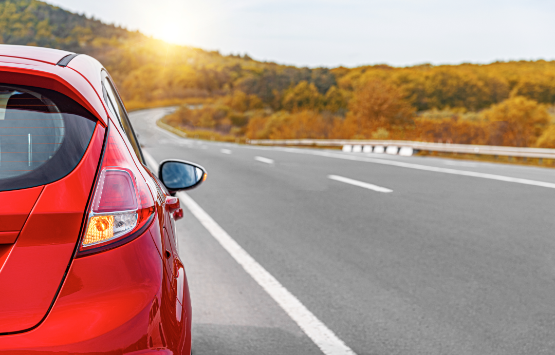 Red car driving on a winding road through a scenic landscape