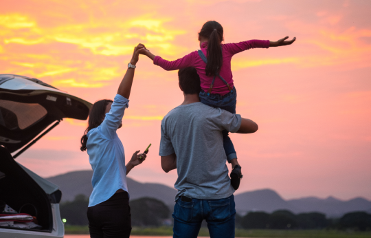 Famliy enjoying sunset near a car child on parents shoulders