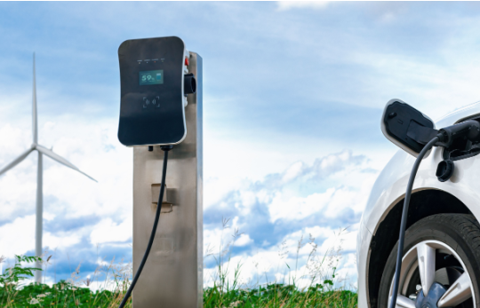 kablosu elektrikli araca bağlı Elektrikli araç şarj ünitesi ve arkasında rüzgar gülü