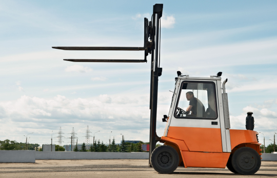 Açık alanda yük kaldıran turuncu forklift ve operatör