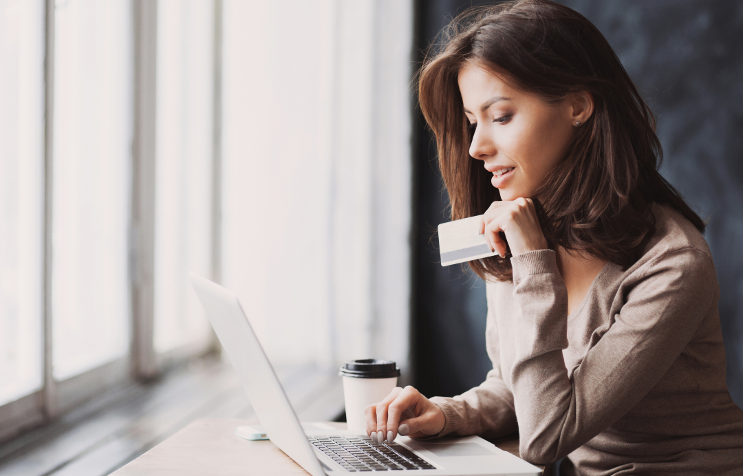 Woman shopping online with credit card on laptop by window