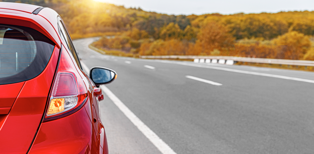Red car driving on a winding road through a scenic landscape