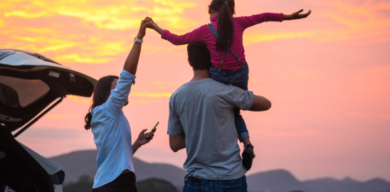 Famliy enjoying sunset near a car child on parents shoulders