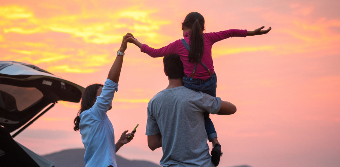 Famliy enjoying sunset near a car child on parents shoulders