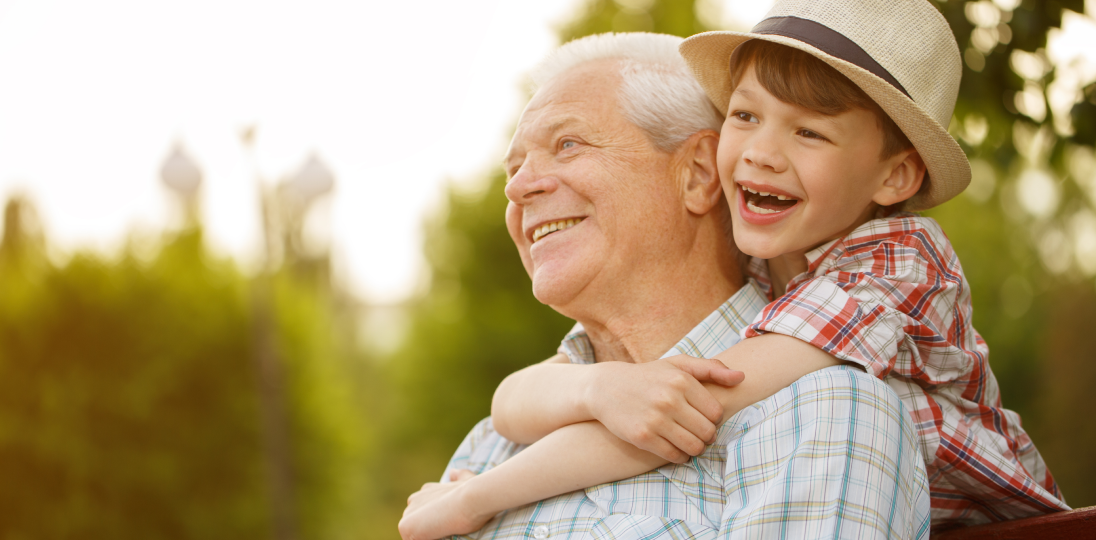 Child hugging smiling elderly man outdoors repsenting family care