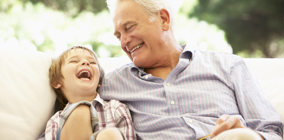 Grandfather and child launghing together outdoors on a sofa