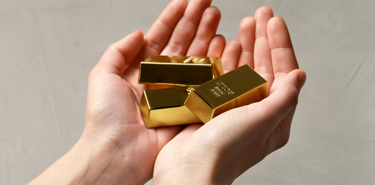 Hand holding several gold bars against a plain background