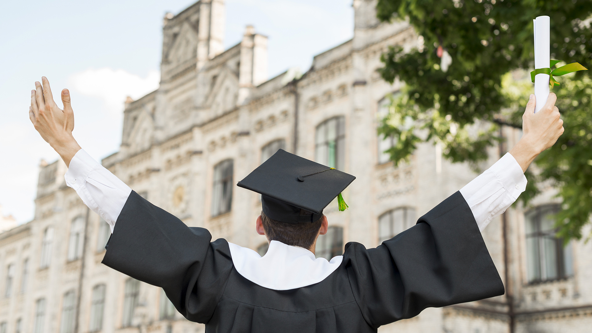 A young person in front of a university building with their arms outstretched wearing a graduation cap and gown and a young man in a gown holding his diploma