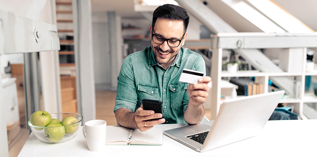 bilgisayar başında telefonuyla kredi kartıyla işlem yapan erkek müşteri